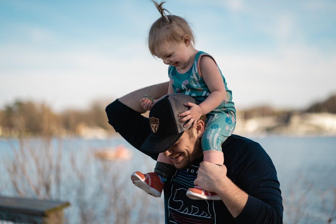 Man in black long sleeve carrying a toddler on his shoulders