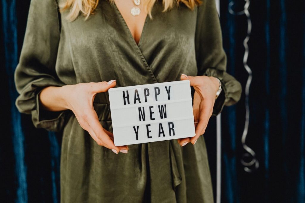 Woman holding a lightbox sign that reads ‘Happy New Year’ against a festive background.